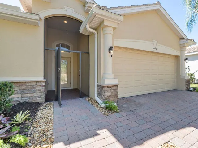 View of exterior entry featuring decorative driveway, an attached garage, stone siding, and stucco siding
