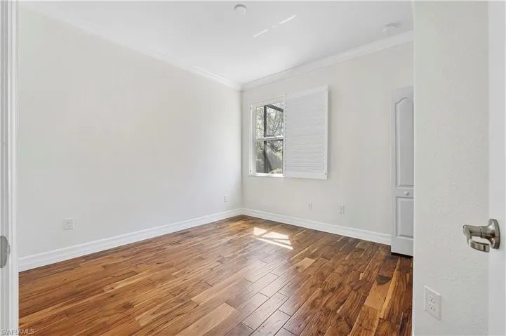 Empty room featuring crown molding, baseboards, and wood finished floors