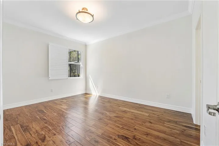 Unfurnished room featuring dark wood finished floors, baseboards, and ornamental molding