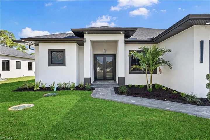 View of exterior entry featuring french doors, a lawn, stucco siding, and roof with shingles