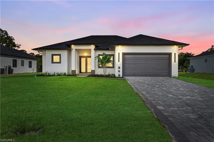Prairie-style house featuring a lawn, decorative driveway, an attached garage, and stucco siding