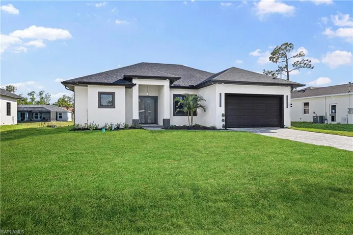 Prairie-style home featuring a front yard, stucco siding, a garage, and decorative driveway