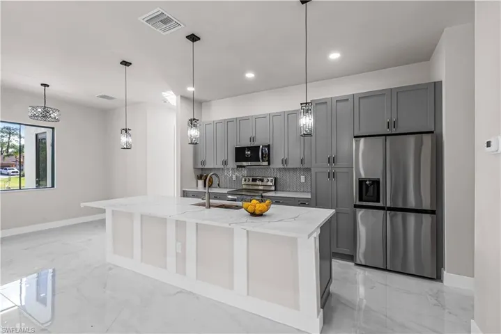 Kitchen featuring stainless steel appliances, gray cabinetry, light stone counters, hanging light fixtures, and decorative backsplash
