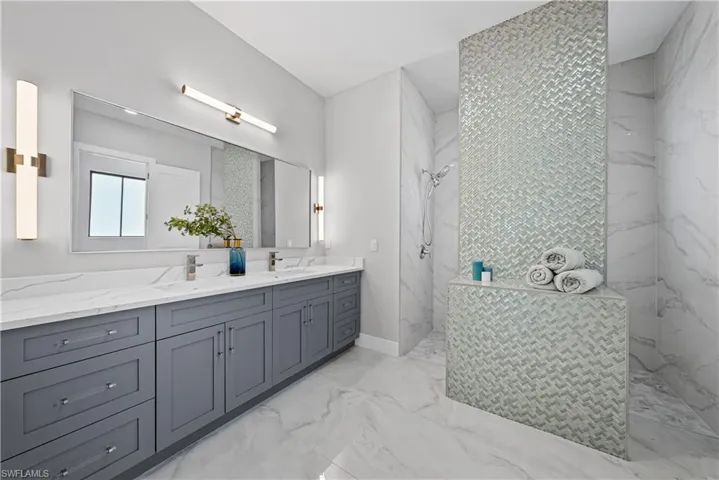 Full bathroom with a marble finish shower, double vanity, and light marble finish floors