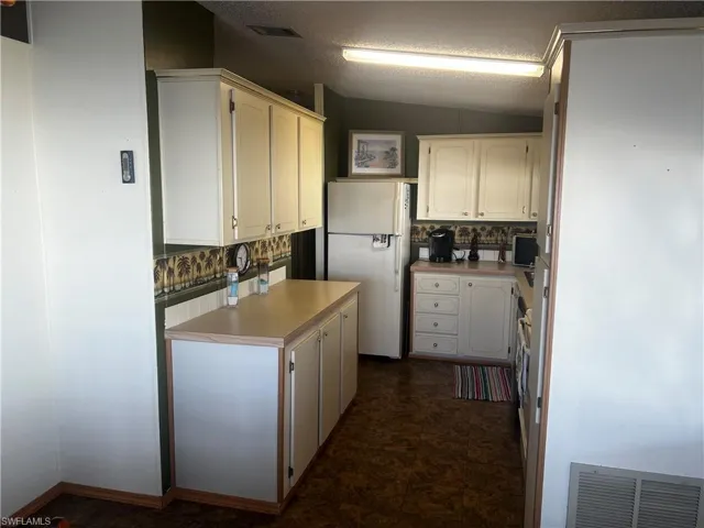 Kitchen featuring light countertops, freestanding refrigerator, white cabinets, and decorative backsplash