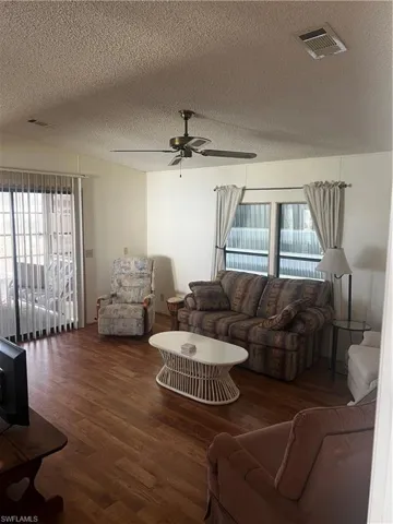 Living room featuring a textured ceiling, a ceiling fan, and wood finished floors