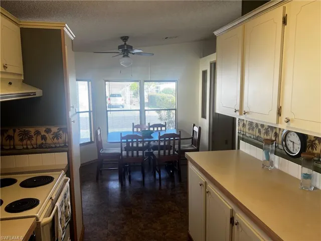 Kitchen featuring a textured ceiling, light countertops, electric range, ventilation hood, and a ceiling fan