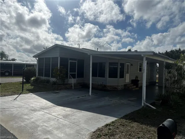 Back of house featuring entry steps, a carport, a sunroom, a patio, and concrete driveway
