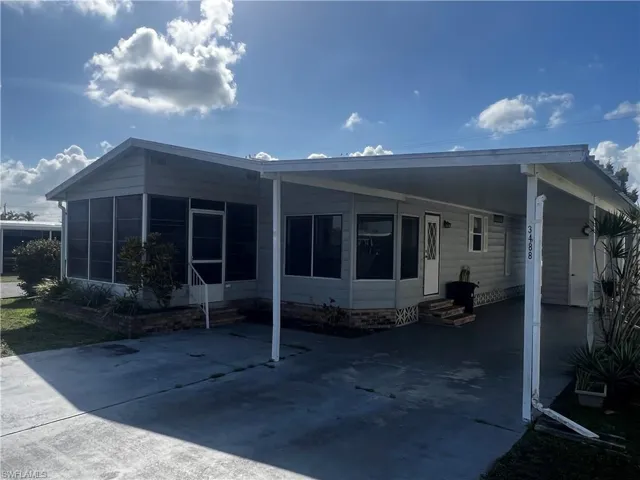 Back of house featuring entry steps, an attached carport, a sunroom, and concrete driveway