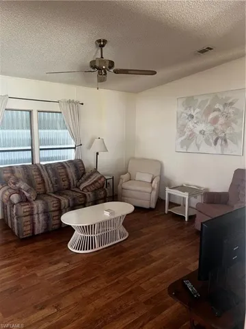 Living area featuring a textured ceiling, a ceiling fan, and dark wood-style flooring