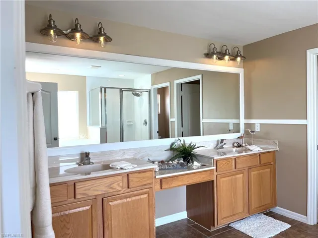 Bathroom featuring a shower stall, double vanity, and dark tile patterned flooring
