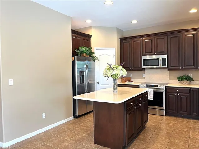 Kitchen featuring dark wood finish cabinetry, stainless steel appliances, a center island, recessed lighting, and light tile patterned floors