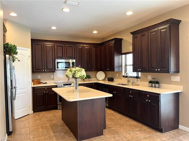 Kitchen with dark wood finish cabinetry, stainless steel appliances, light tile patterned floors, recessed lighting, and light stone countertops