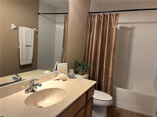 Full bath featuring vanity, shower / tub combo with curtain, and dark tile patterned floors