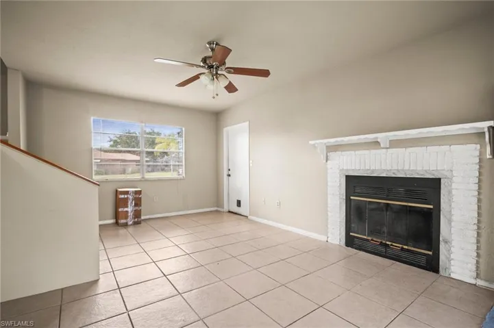 Unfurnished living room with light tile patterned flooring, baseboards, a fireplace, and ceiling fan