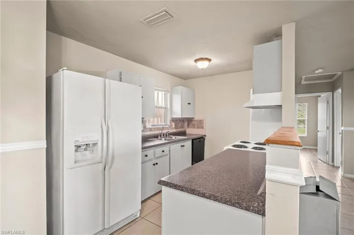 Kitchen featuring visible vents, dark countertops, white fridge with ice dispenser, black dishwasher, and light tile patterned floors