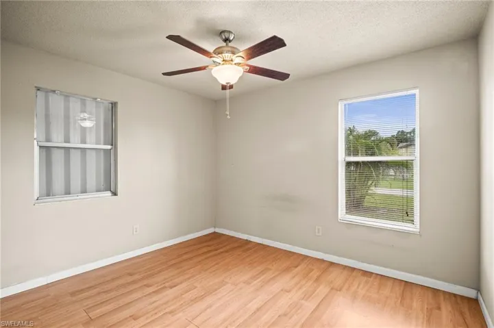 Empty room with a textured ceiling, wood finished floors, baseboards, and a ceiling fan