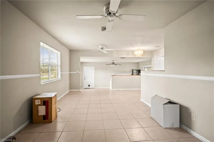 Empty room featuring light tile patterned floors, ceiling fan with notable chandelier, baseboards, and visible vents