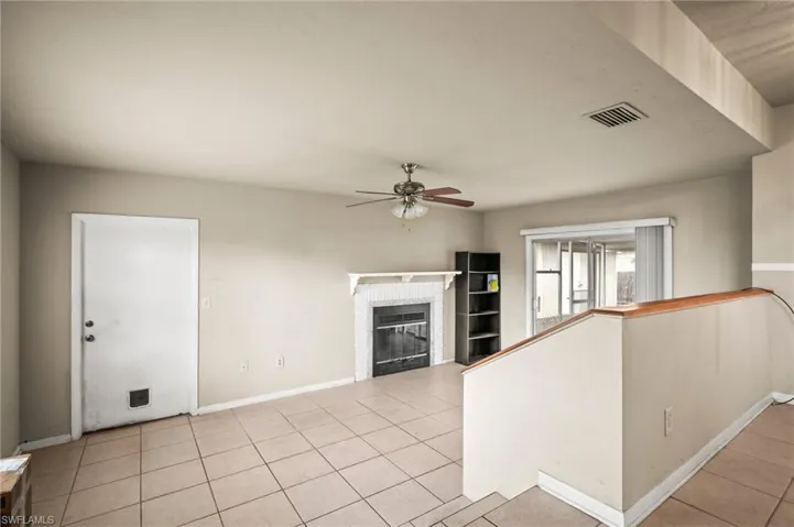 Unfurnished living room featuring visible vents, ceiling fan, a glass covered fireplace, and light tile patterned floors
