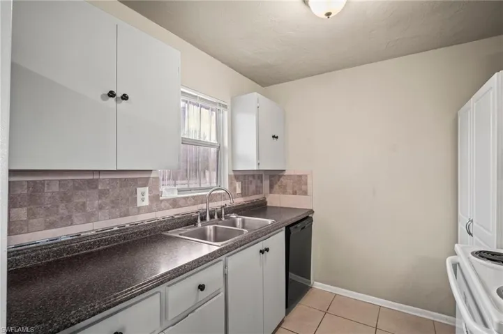 Kitchen featuring white electric range oven, backsplash, a sink, dark countertops, and dishwasher
