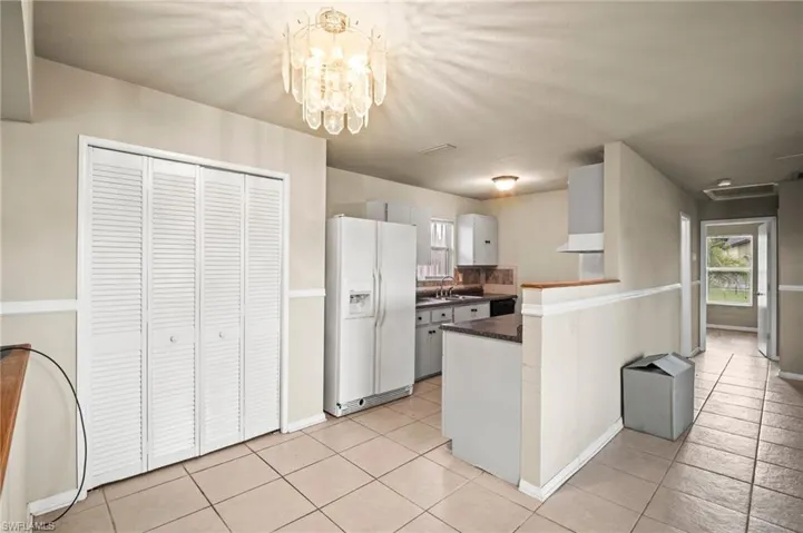 Kitchen with dark countertops, white fridge with ice dispenser, a sink, and light tile patterned floors