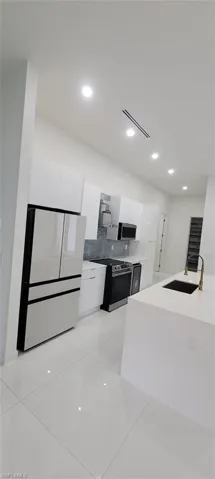 Kitchen with appliances with stainless steel finishes, white cabinets, backsplash, sink, and light tile floors