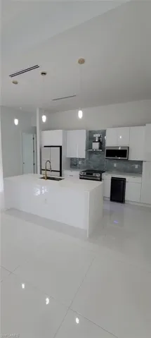 Kitchen with stainless steel appliances, decorative light fixtures, backsplash, sink, and white cabinetry