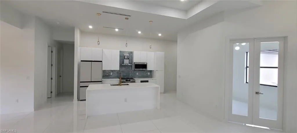 Kitchen with tasteful backsplash, fridge, an island with sink, wall chimney exhaust hood, and white cabinets