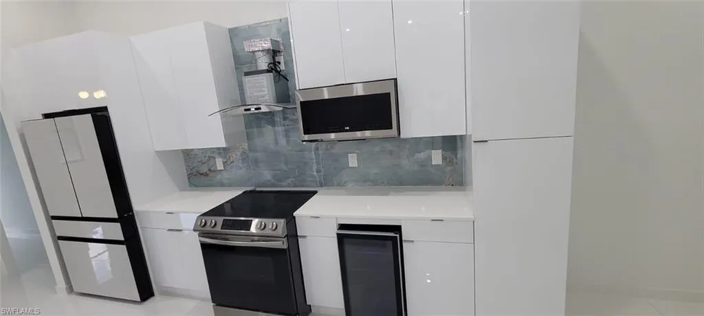 Kitchen with stainless steel appliances, exhaust hood, tasteful backsplash, white cabinets, and light tile floors
