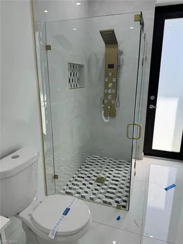 Bathroom with a shower with shower door, tile flooring, and toilet
