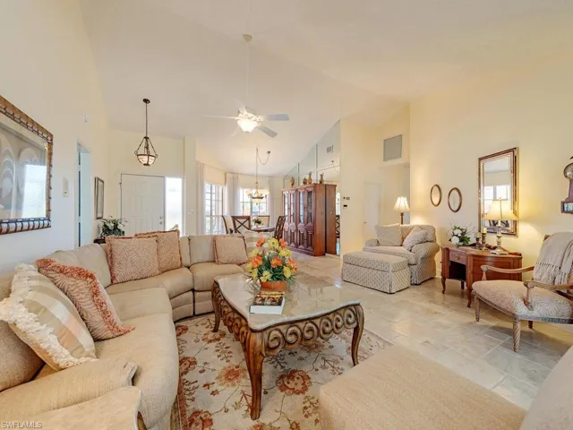 Living area featuring high vaulted ceiling, a ceiling fan, a chandelier, and stone finish floors
