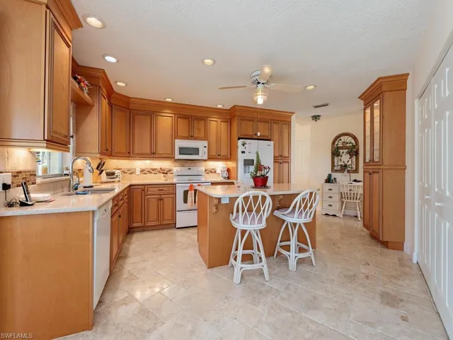 Kitchen featuring white appliances, a breakfast bar area, brown cabinetry, a center island, and stone tile floors