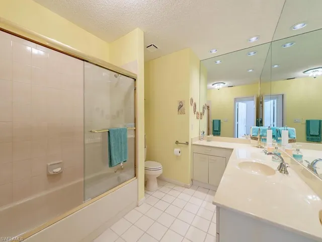 Full bathroom featuring double vanity, combined bath / shower with glass door, light tile patterned floors, and a textured ceiling
