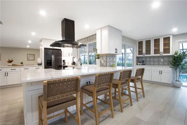 Kitchen with white cabinetry, island range hood, a kitchen breakfast bar, and stainless steel fridge with ice dispenser