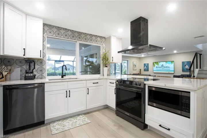 Kitchen featuring sink, island range hood, appliances with stainless steel finishes, kitchen peninsula, and white cabinets