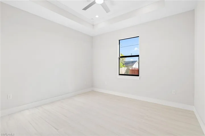 Spare room featuring a tray ceiling, a ceiling fan, and light floors