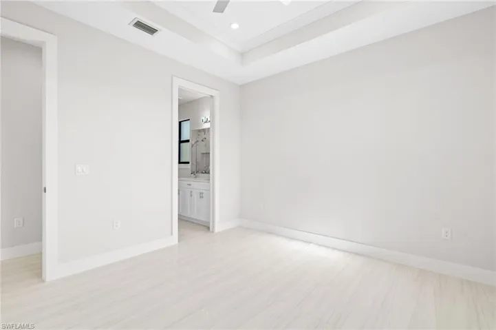 Unfurnished bedroom with ceiling fan, a raised ceiling, ensuite bathroom, crown molding, and recessed lighting