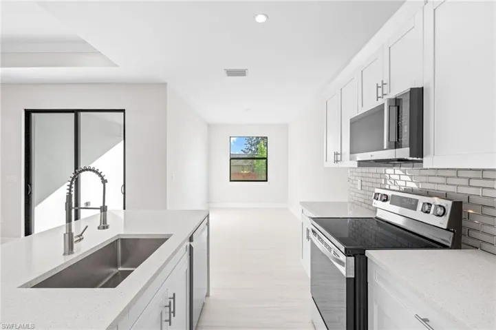 Kitchen featuring stainless steel appliances, white cabinetry, light stone countertops, recessed lighting, and decorative backsplash