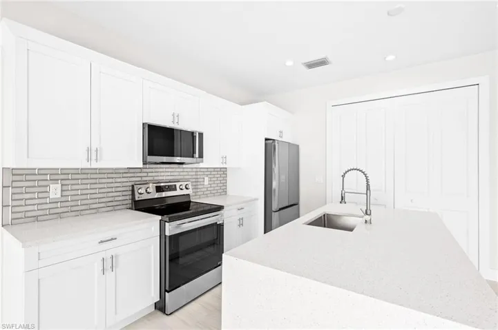 Kitchen featuring stainless steel appliances, light stone counters, white cabinets, and recessed lighting