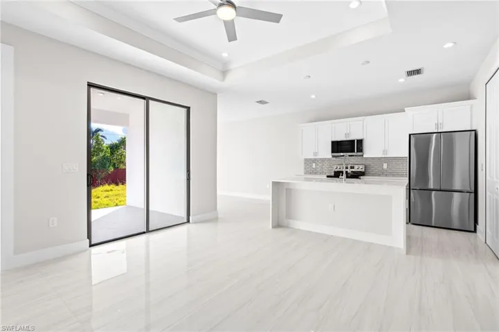 Kitchen with stainless steel appliances, a center island with sink, white cabinetry, a raised ceiling, and recessed lighting