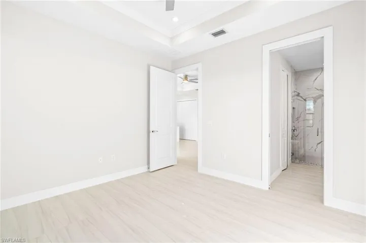 Unfurnished bedroom featuring a ceiling fan, a raised ceiling, connected bathroom, and recessed lighting