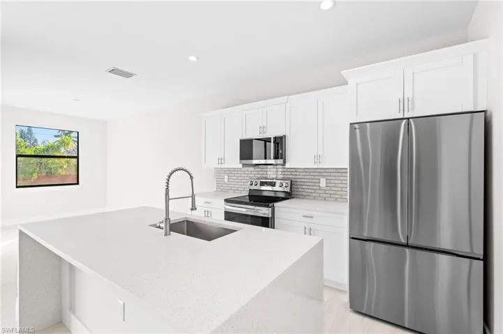 Kitchen featuring stainless steel appliances, light stone countertops, white cabinets, a kitchen island with sink, and decorative backsplash