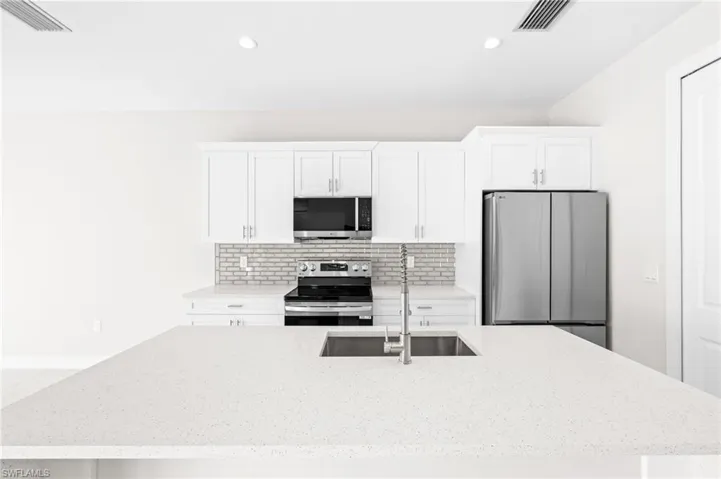 Kitchen with stainless steel appliances, an island with sink, light stone countertops, white cabinets, and recessed lighting