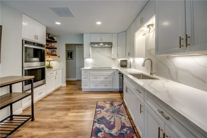 Kitchen with light hardwood / wood-style floors, appliances with stainless steel finishes, light stone counters, backsplash, and sink