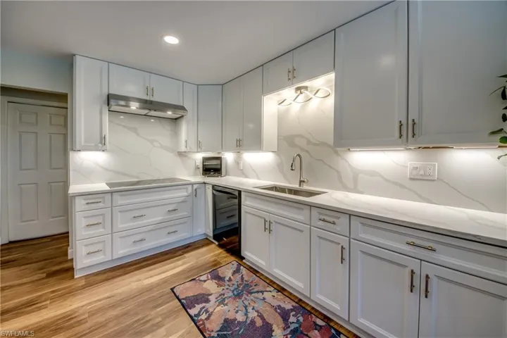 Kitchen featuring sink, tasteful quartz backsplash, black electric cooktop, and light luxury vinyl hardwood style  flooring