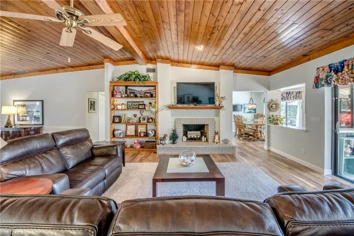 Living room with ceiling fan, vaulted ceiling, a fireplace, light wood-type flooring, and wooden ceiling