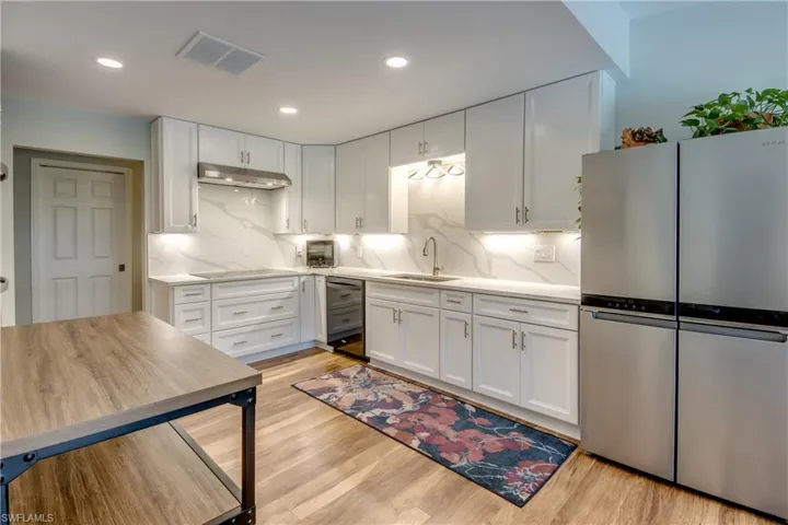 Kitchen with backsplash, stainless steel refrigerator, sink, and light wood-type flooring