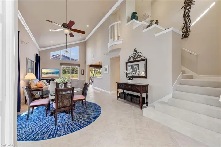 Dining room with high vaulted ceiling, stairway, a ceiling fan, light tile patterned floors, and crown molding