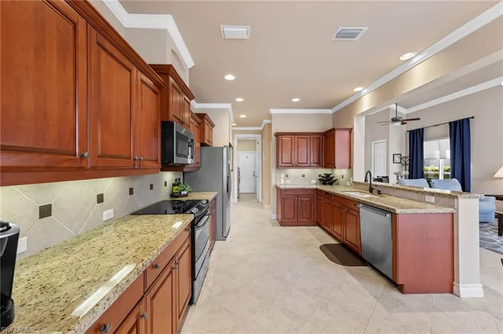 Kitchen featuring ornamental molding, stainless steel appliances, light stone countertops, a peninsula, and backsplash