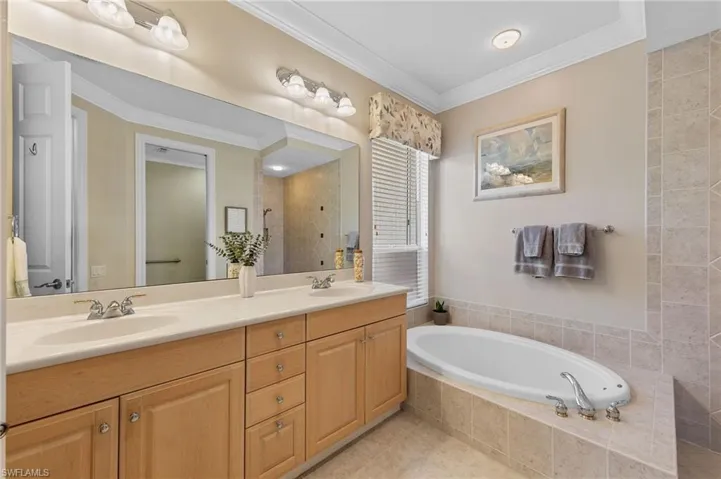 Bathroom featuring a bath, double vanity, crown molding, and tiled shower